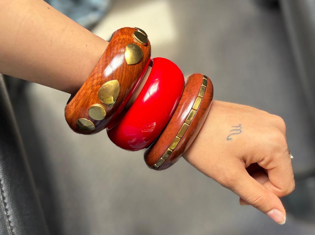 Hand wearing two wooden bangles with gold accents on a blurred background